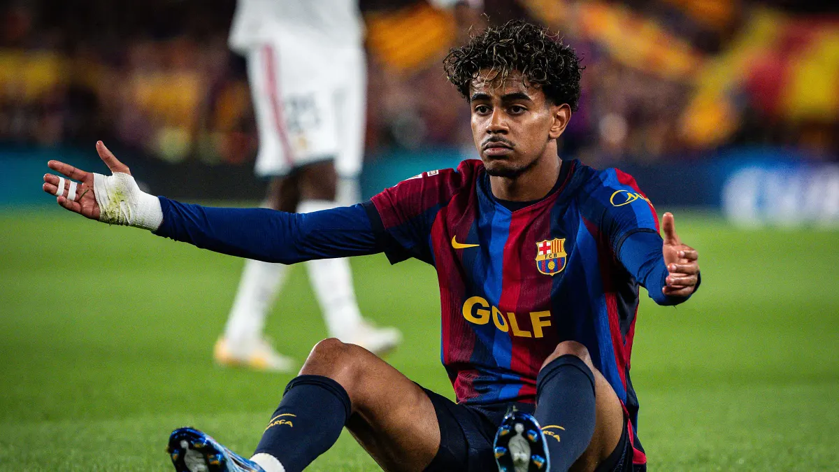 Futbolista del FC Barcelona sentado sobre el césped con los brazos abiertos durante un partido.